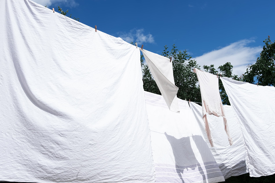 White cotton bed linens hung out to dry on a sunny day.
